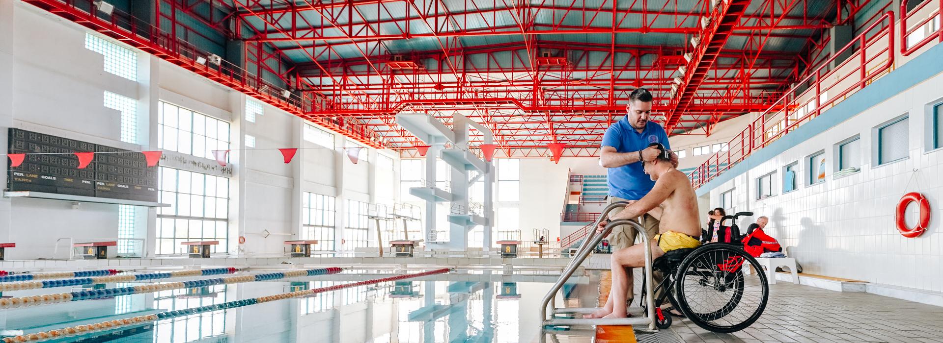 Cover. Indoor shot of Universities swimming facilities, a wheelchair user is getting into the pool assisted by "Perpato" staff.